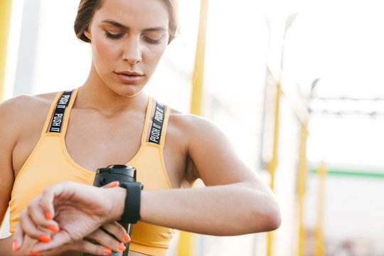 Image of concentrated woman looking at smartwatch while walking outdoors