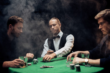 croupier holding playing cards near men on black with smoke