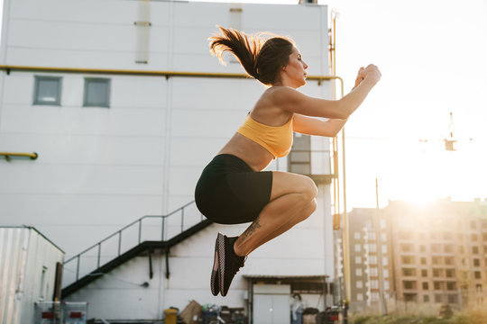 Image of woman in sportswear jumping while doing crunches outdoors