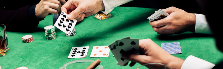 panoramic shot of men playing poker near poker table