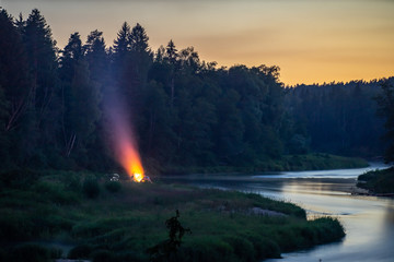 Evening time. Bonfire near the forest and the river.
