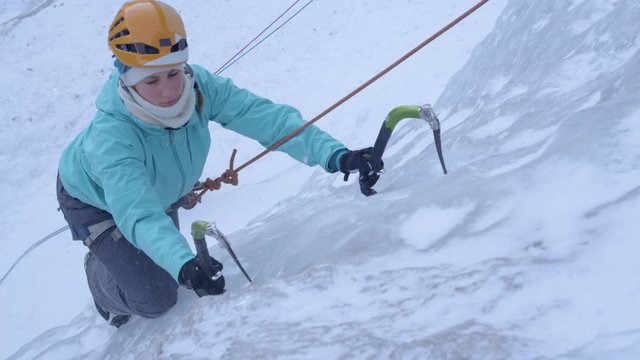 Slow motion close up cinematic shot of a woman sticking her icepicks into the icy waterfall while climbing up the towering mountain in Slovenia