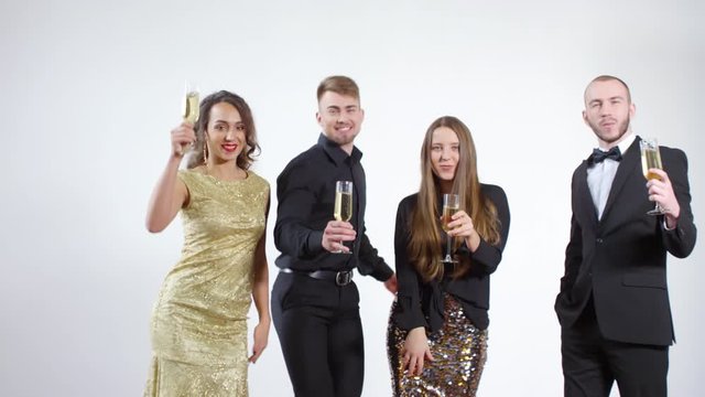 Slowmo shot of happy young men and women holding glasses of champagne and dancing isolated on grey background