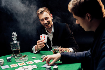 selective focus of happy man holding playing cards on black with smoke
