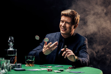 cheerful man throwing in air poker chips and cigar on black with smoke