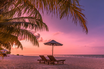 Twilight sky, sunrise or sunset beach view. Two loungers and umbrella under palm leaves. Luxury summer vacation background. Inspirational beach view, wonderful scenery