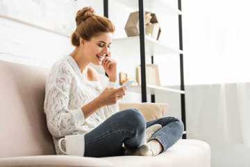 attractive woman in white sweater smiling and using smartphone