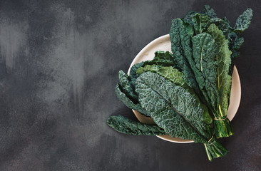 Fresh  Tuscan kale leaves on a white plate and on rustic dark background. Top view, blank space