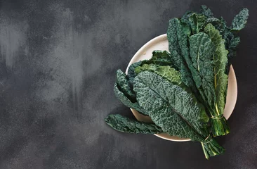 Poster Fresh  Tuscan kale leaves on a white plate and on rustic dark background. Top view, blank space © happyimages