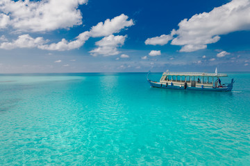 Traditional boat in Maldives, Dhoni in blue turquoise sea under blue sky with white fluffy clouds. Exotic view of tropical paradise