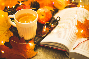 Autumn mood, still life cup of tea with lemon, yellow maple leaves and red, an apple, with a plaid, an open book on a wooden background. Top view, cozy house. flat lay