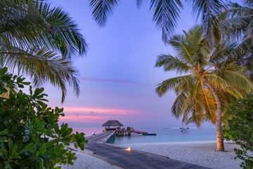 Maldives resort island in sunset with wooden jetty, amazing colorful sky. Perfect sunset beach...