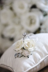 diamond wedding ring on a white silk pillow with roses in the background