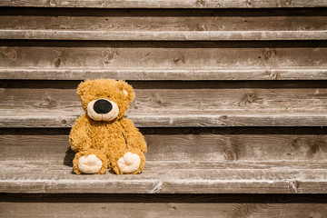 A lone Teddy bear sits on a wooden staircase.