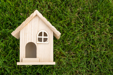 Flat lay view of little wooden house on green grass for real estate property concept