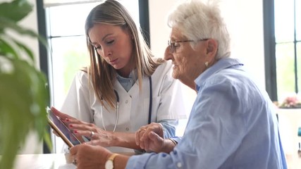 Elderly woman with nurse at home looking at tablet - Powered by Adobe