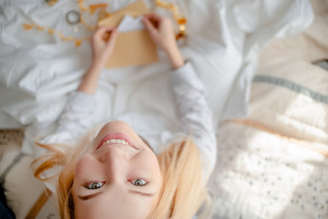 Smiling blond girl with an envelope sitting on a bed. Top horizontal view  christmas and  new year concept