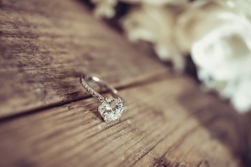 Beautiful toned picture with diamond wedding ring on a wooden surface against the background of a bouquet of flowers