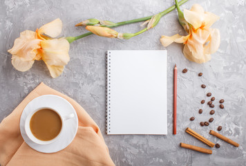 Orange iris flowers and a cup of coffee with notebook on a gray concrete background.