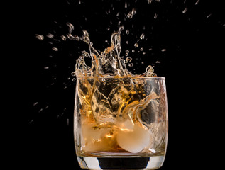 Drops of ice in a glass with whiskey on a black background, splashes and drops