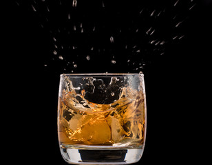 Drops of ice in a glass with whiskey on a black background, splashes and drops