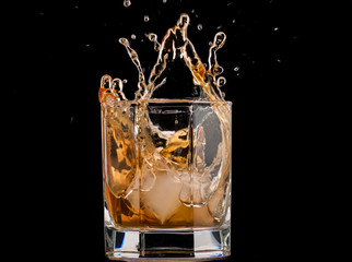 Drops of ice in a glass with whiskey on a black background, splashes and drops