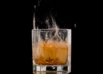 Drops of ice in a glass with whiskey on a black background, splashes and drops