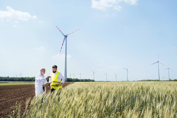 Engineers standing on wind farm, making notes.