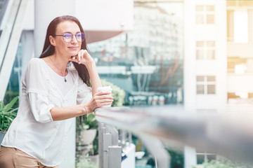 Fototapeta premium Start of the day. Beautiful mature woman drinking a cup of coffee on a terrace. Copy space on the right side