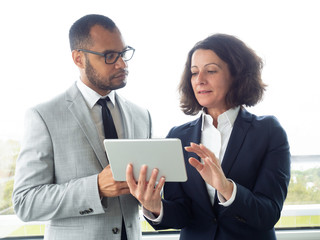 Focused business colleagues using digital tablet. Multiethnic businessman and businesswoman standing and working with tablet pc in office. Business and technology concept
