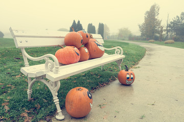 Many pumpinks with painted faces on white porch.