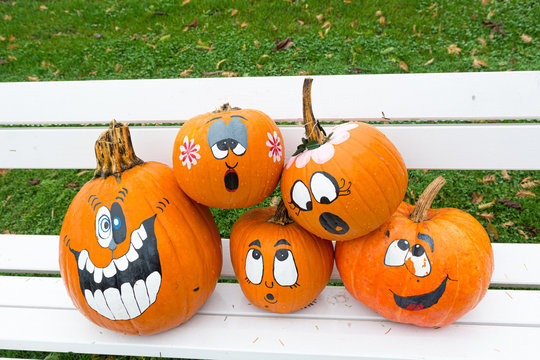 Many pumpinks with painted faces on white porch.