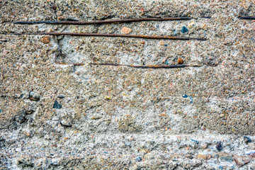 Texture of crumbling concrete wall with horizontal bars of rusty iron armature. Through damage in old rough concrete surface with small stones, details of internal reinforcement are visible
