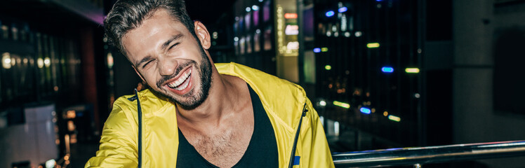 panoramic shot of handsome man in yellow jacket smiling in night city