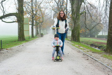 Youg mother walking with her daughter riding a toddler scooter in park.