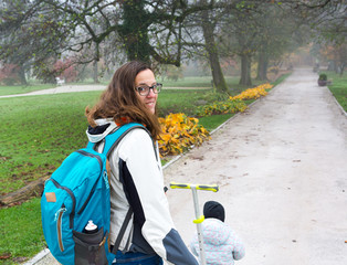 Youg mother walking with her daughter riding a toddler scooter in park.