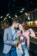 handsome businessman giving bouquet and hugging attractive woman in night city