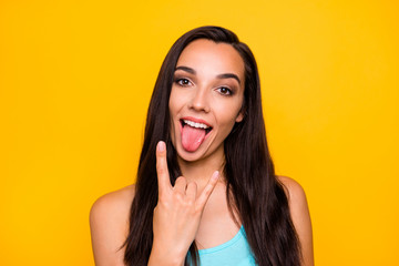 Close up photo of playful girlish feminine young rocker sticking tongue out with fingers horned showing her love for metal isolated over vivid color yellow background