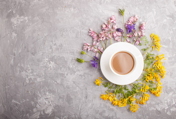 Yellow, pink and blue flowers in a spiral and a cup of coffee on a gray concrete background. top view.