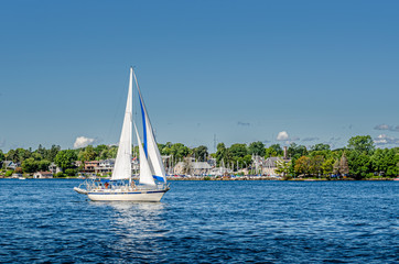 Sailboat sailing past yacht club shoreline