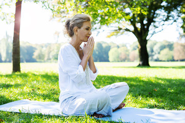 Positive Frau im mittleren Alter macht Meditationsübungen im Park 