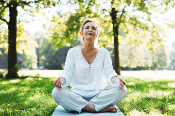 Positive Frau im mittleren Alter macht Meditationsübungen im Park 