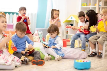 Foto auf Acrylglas Tagesbetreuung Kindergärtnerin mit Kindern im Musikunterricht in der Kindertagesstätte. Kleinkinder spielen zusammen mit Entwicklungsspielzeug.