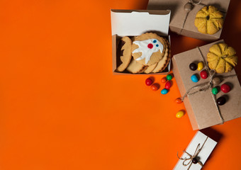 The Concept Of Halloween. Gift boxes, homemade cookies with scary ghosts and bats, colorful candies on an orange background. Free space for your text.