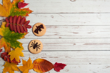 The concept of Halloween. Scary delicious homemade cookies with bats and spiders, colorful autumn leaves on a light wooden background. Free space for your text.