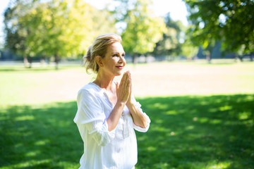 Eine attraktive Best-Ager Frau macht Meditations-Übungen im Park 