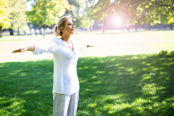 Fototapeta premium Eine attraktive Best-Ager Frau macht Meditations-Übungen im Park 