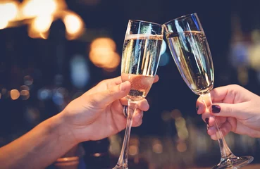 Fotobehang Twee glazen met mousserende champagnewijn in handen, concept voor vakantie, huwelijksvalentijnskaarten Kerstmis en Nieuwjaar, bokeh, in een restaurant en café © olezzo