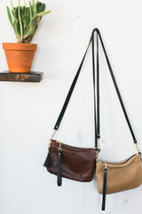 Fototapeta na wymiar Two brown leather bags hanging on wall next to cactus, styled, copy space