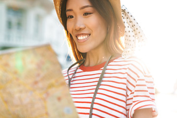 Portrait of young asian tourist woman holding paper map on city street